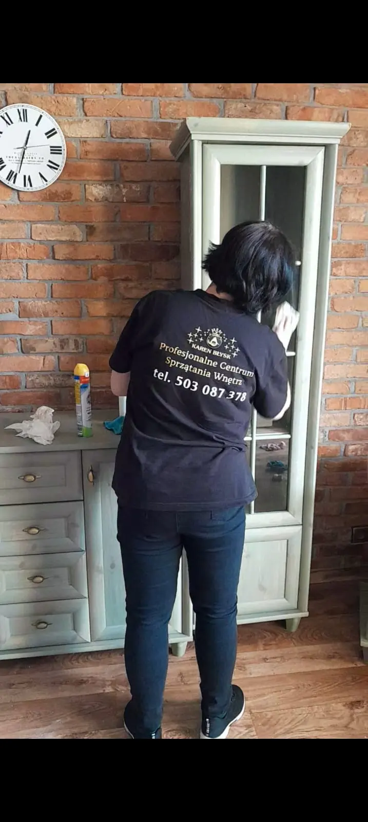 Sprzątaczka czyszcząca witrynkę w salonie – dokładne mycie mebli szklanych i usuwanie kurzu z dekoracji